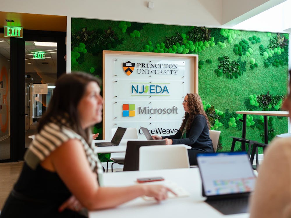Focused on a woman working on her computer, sitting in front of the AI Hub Founding Partners sign.