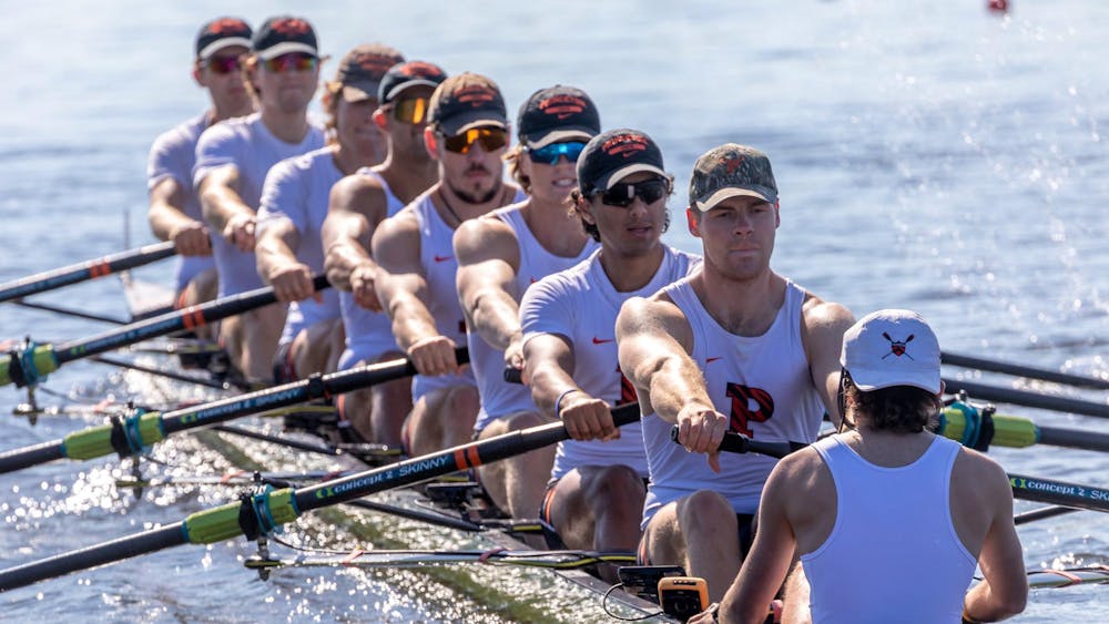 Group of rowers in white and orange jerseys row in unison on the lake.