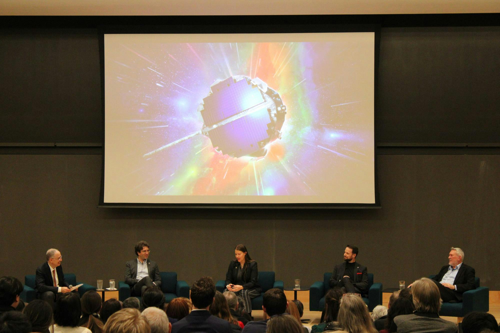 Five people in suits sit in front of a projector showing a space probe.