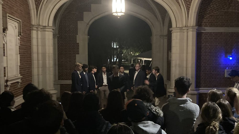 In an arch, at night, a group of formally-dressed men stand in a semi-circle.