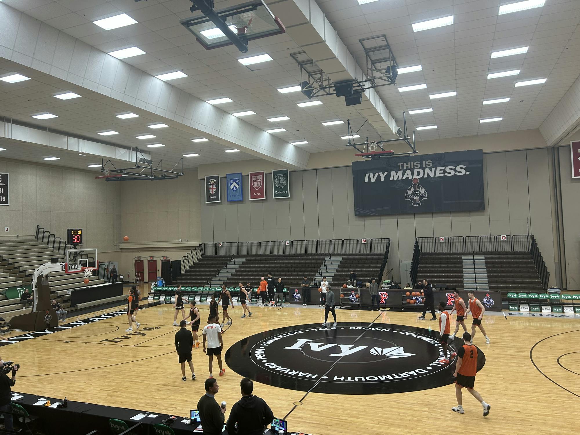 A group of men stand on a basketball court, some shooting at a basket. A black circle with the word "Ivy" is pasted on the middle of the court.