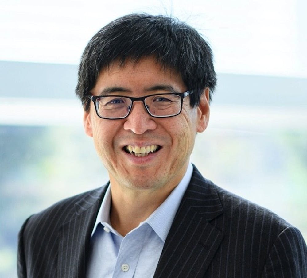 Asian man with glasses smiling in a suit.