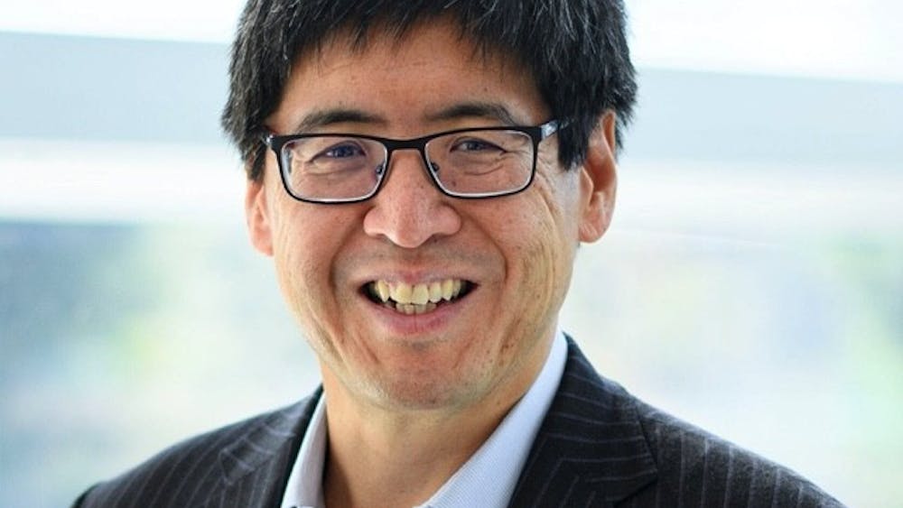 Asian man with glasses smiling in a suit.