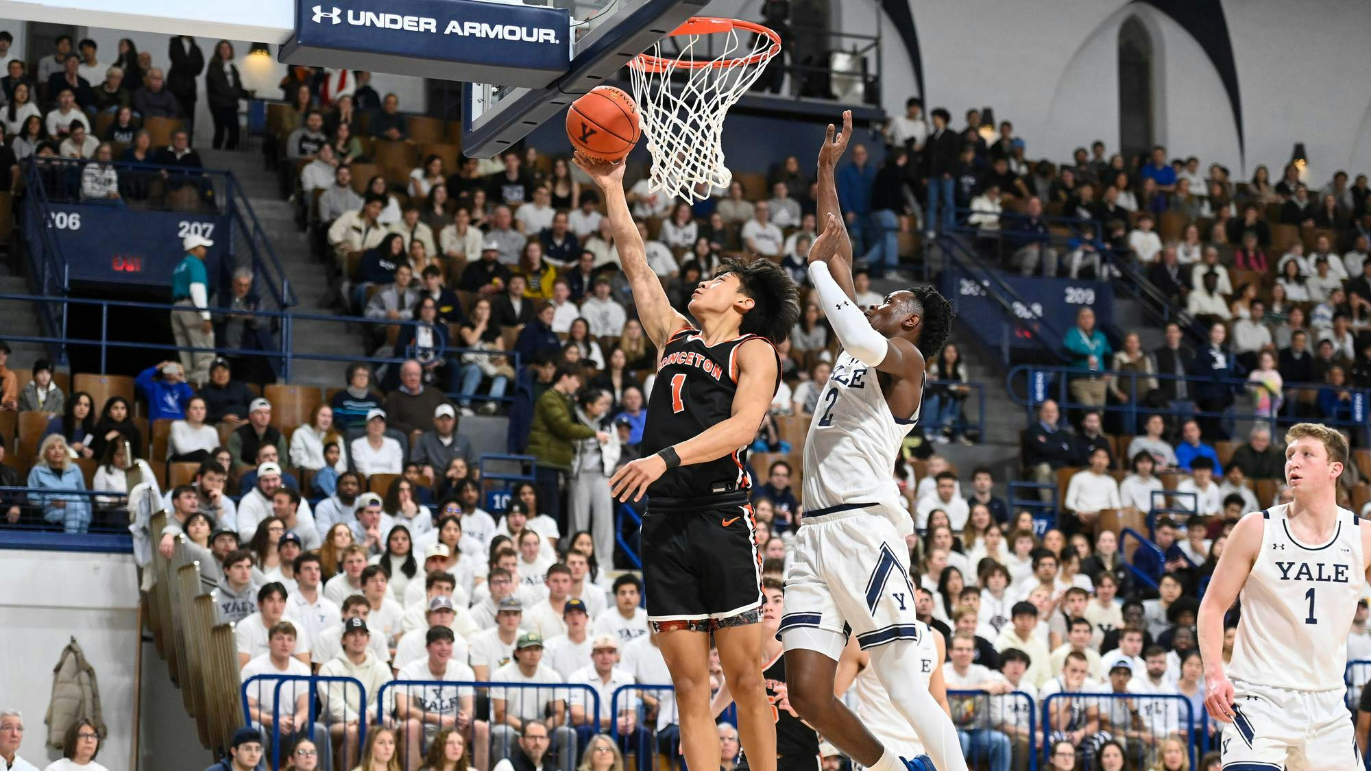 A man in a black basketball jersey attacks the rim as the crowd watches on.