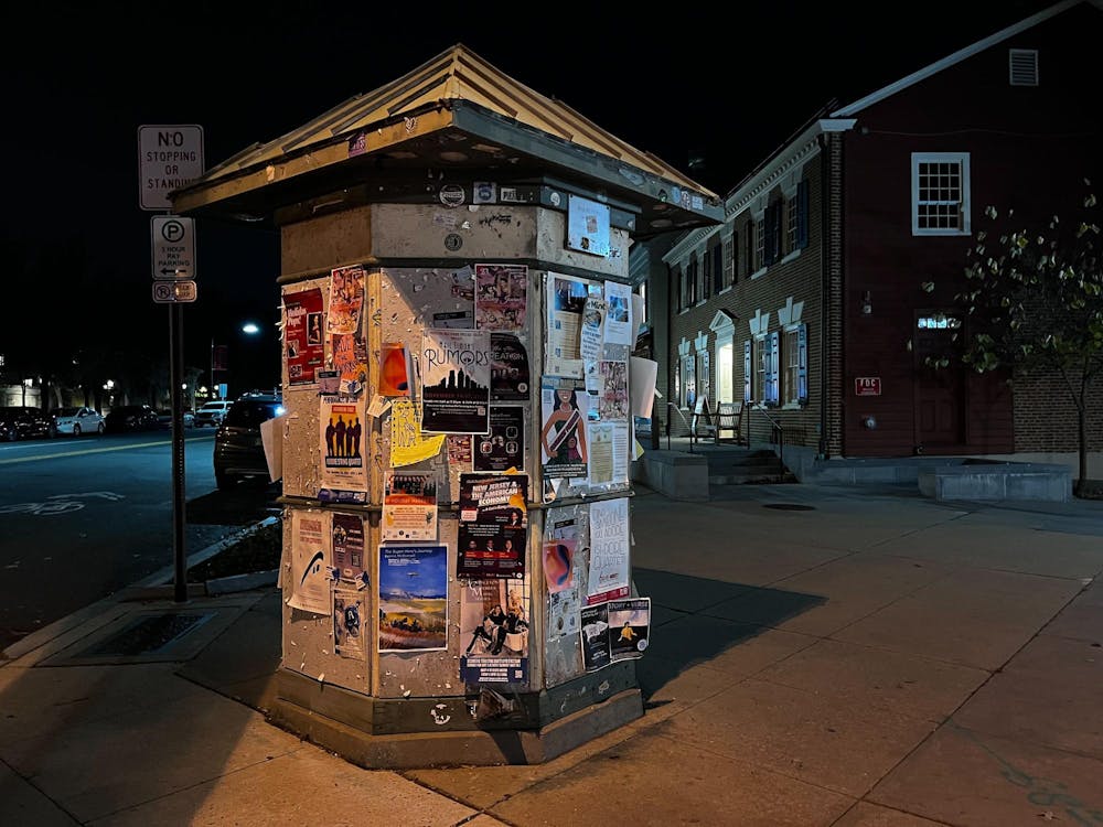 A large column with bulletin boards featuring many posters on the side of a street at night.