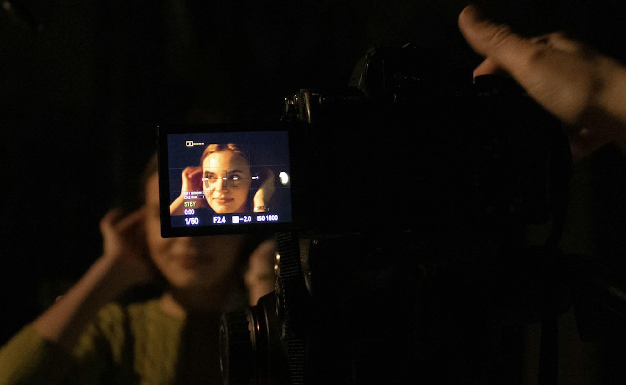 A girl with short blonde hair is seen through the lens of a black camera.