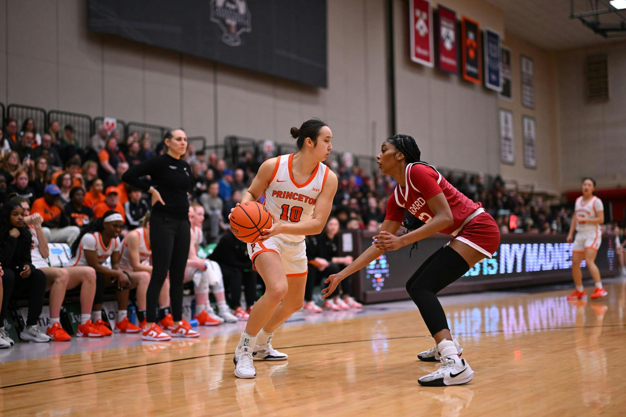 Two women are playing basketball on a court. Behind them is a crowd of people cheering. 