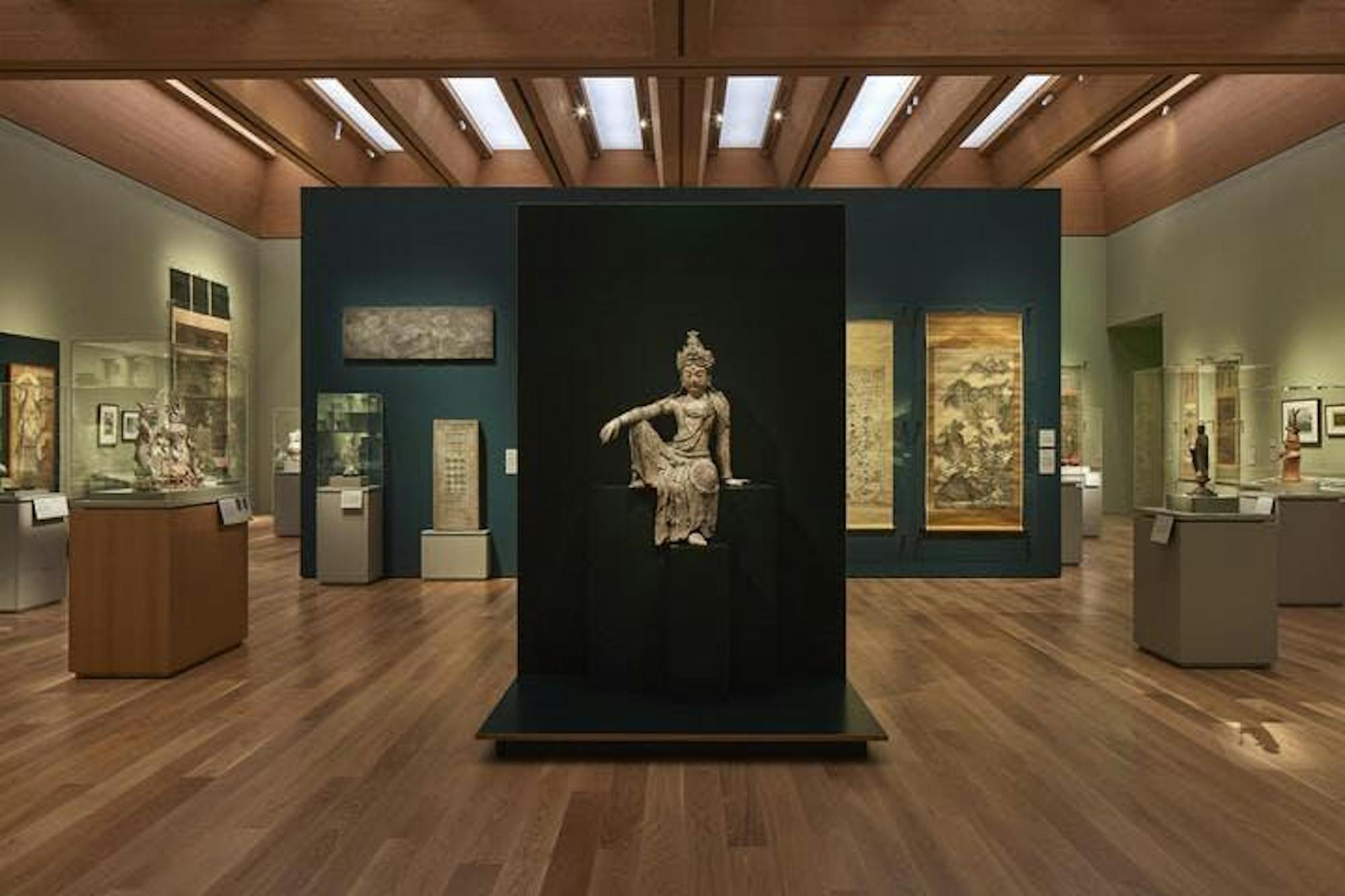 Una escultura se alza frente a una pared oscura. Aldredor de la escultura hay una sala que contiene otras obras de arte.