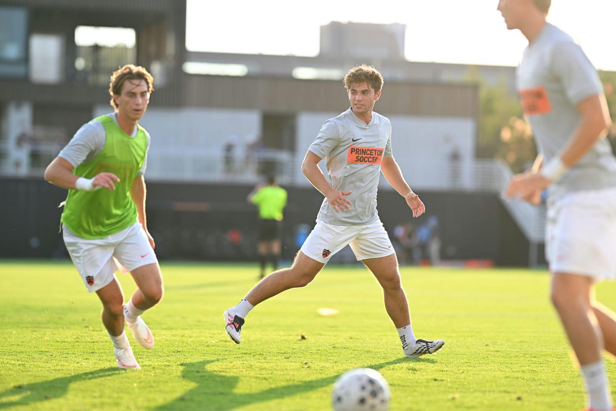 3 men in gray and orange jerseys run on a soccer pitch