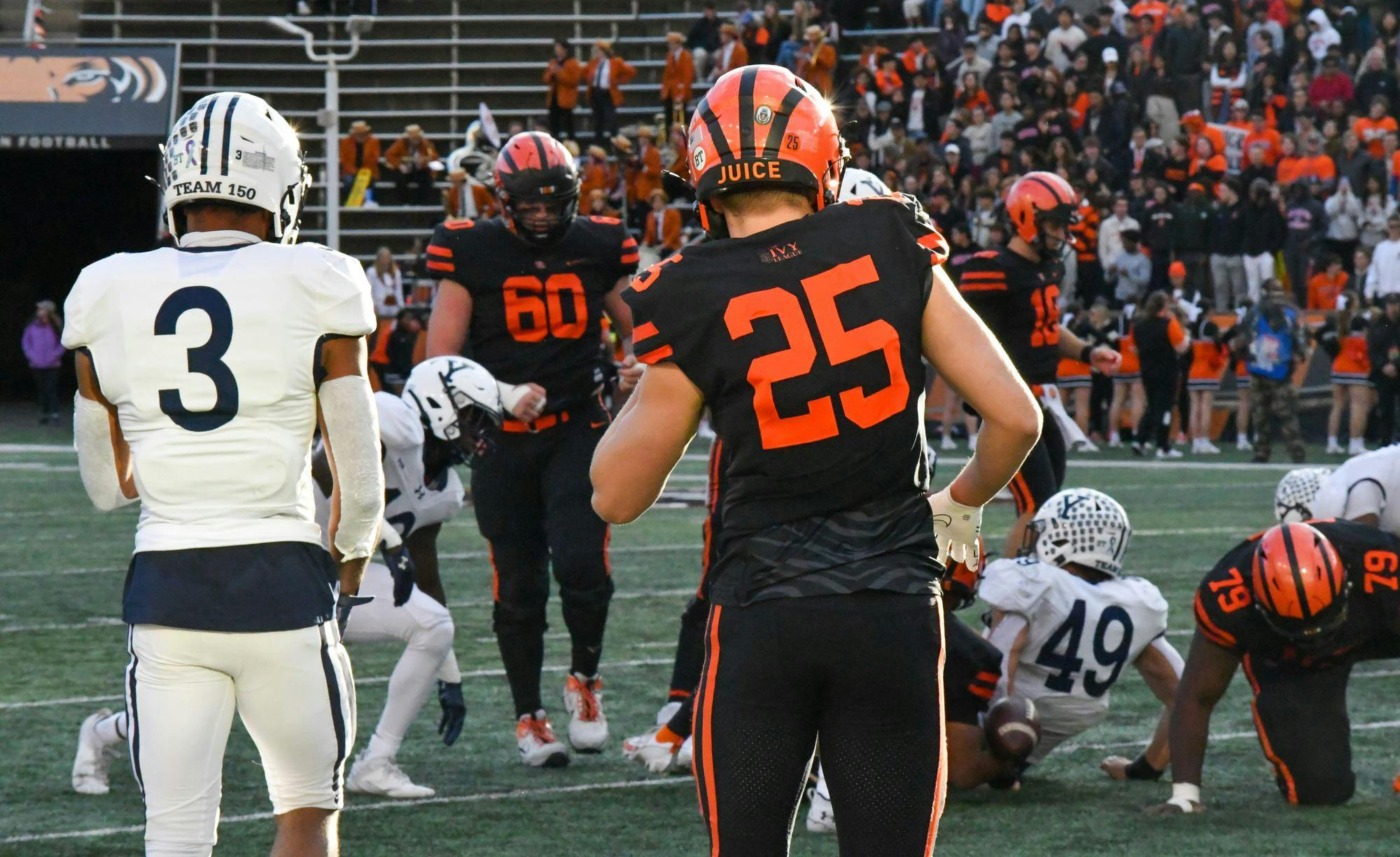 A football player from Princeton with the number 25 and a football player with the number 3 get ready for the next play.