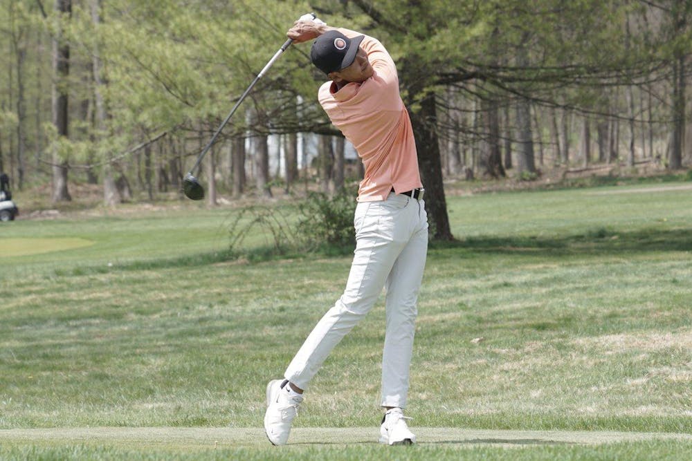 Image of men's golf player in orange polo and tan slacks swinging his club.