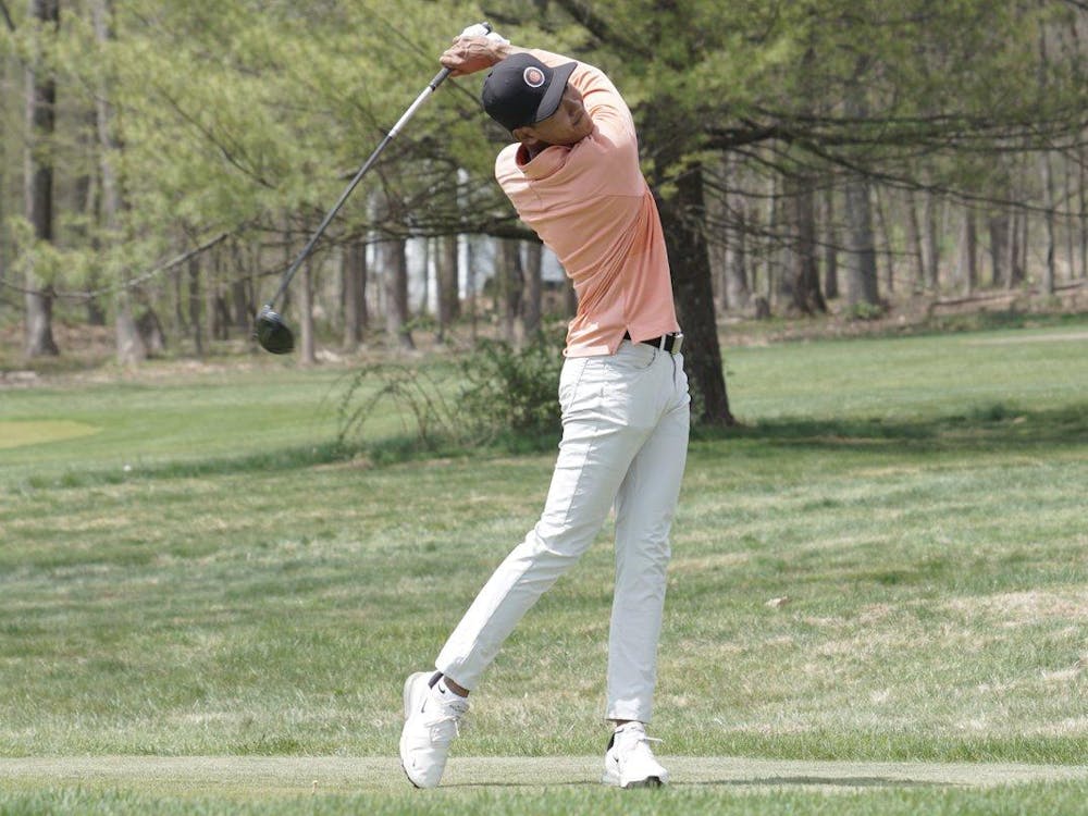 Image of men's golf player in orange polo and tan slacks swinging his club.