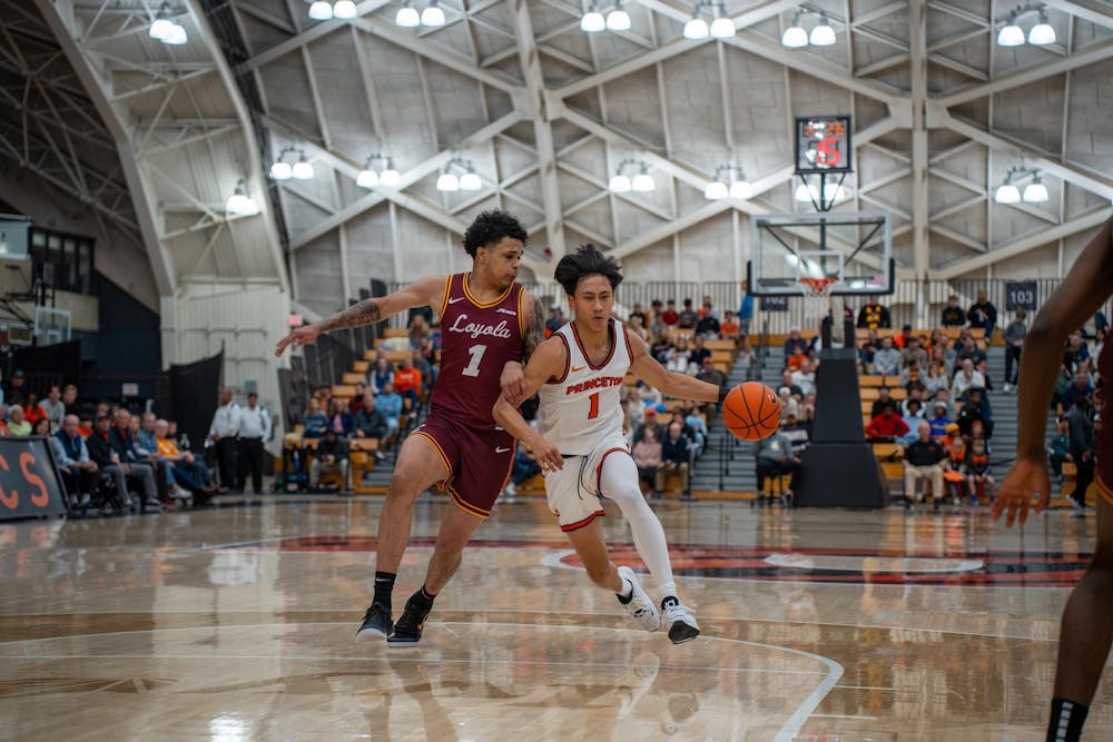 A man wearing a white jersey dribbling a basketball while being defended by a man in a burgundy jersey.