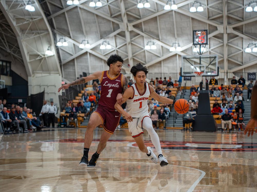A man wearing a white jersey dribbling a basketball while being defended by a man in a burgundy jersey.