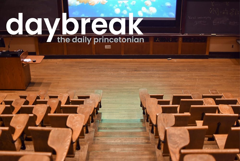 A view of a classroom that has tiered levels of seating. View is from the back of the class, looking down on desks and a screen in front of a blackboard. Text in the top left corner of the image says "Daybreak: the daily princetonian"