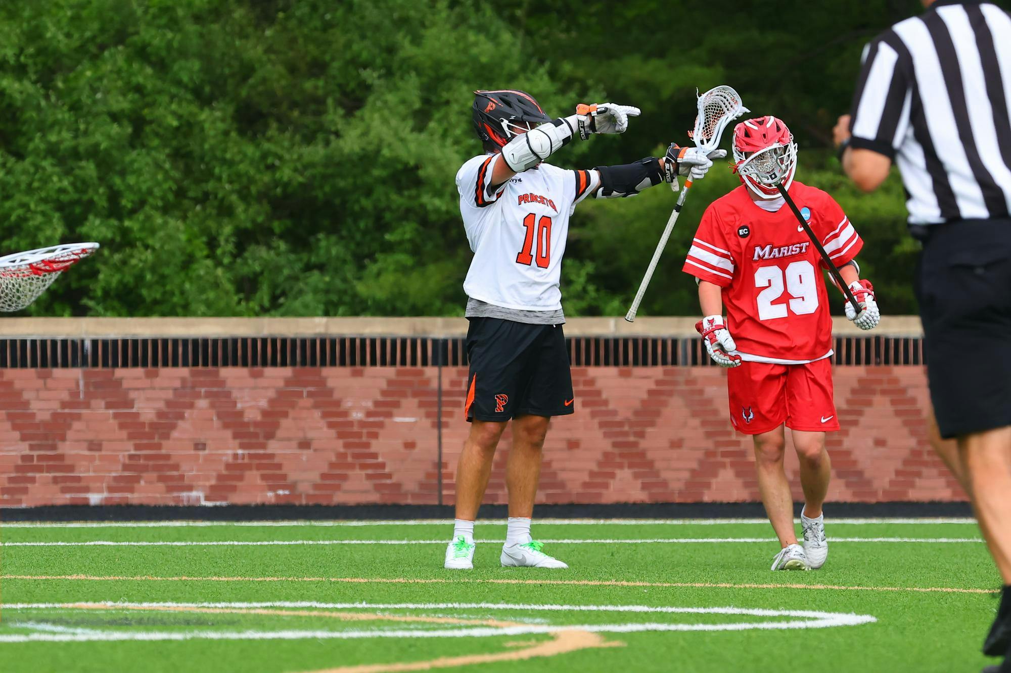 A Princeton lacrosse player wearing black shorts and a white No.10 jersey celebrates on a turf field with a Marist player in red shorts and a red jersey standing beside him.