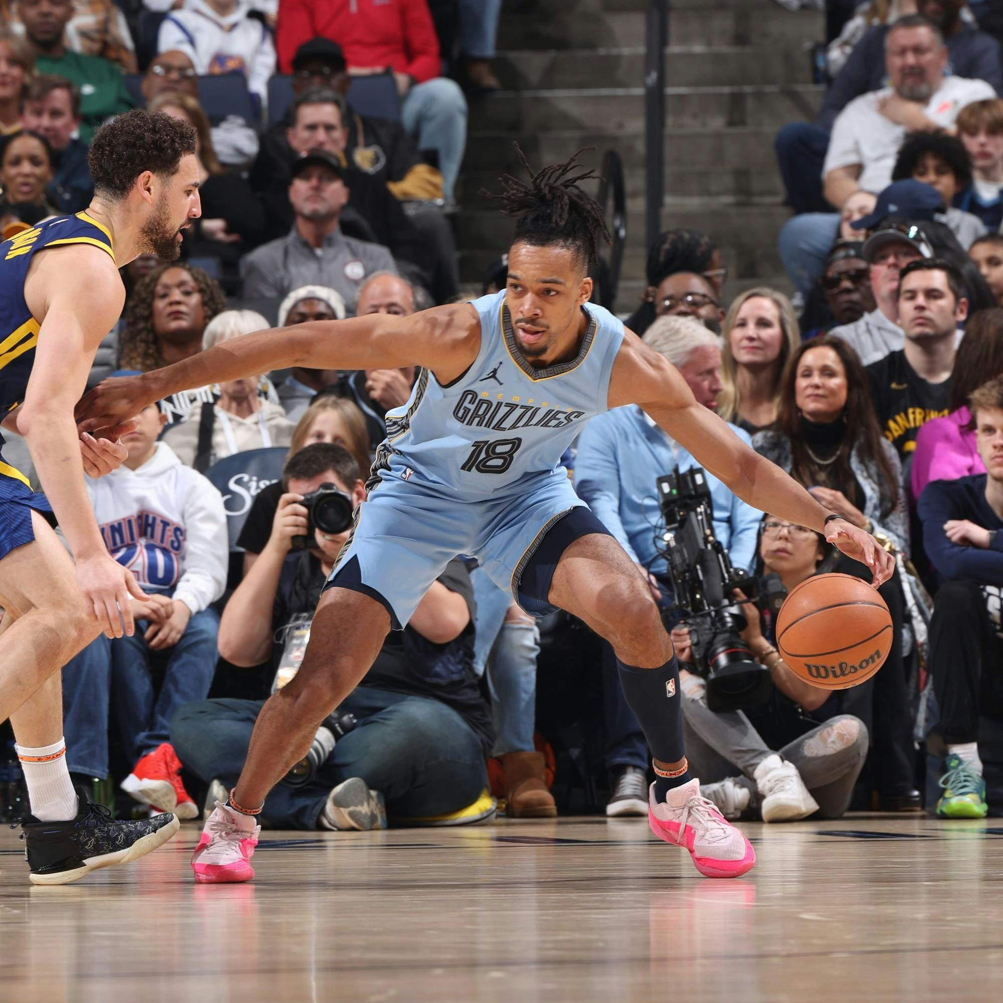 A man dribbling a basketball as he posts up against another player.