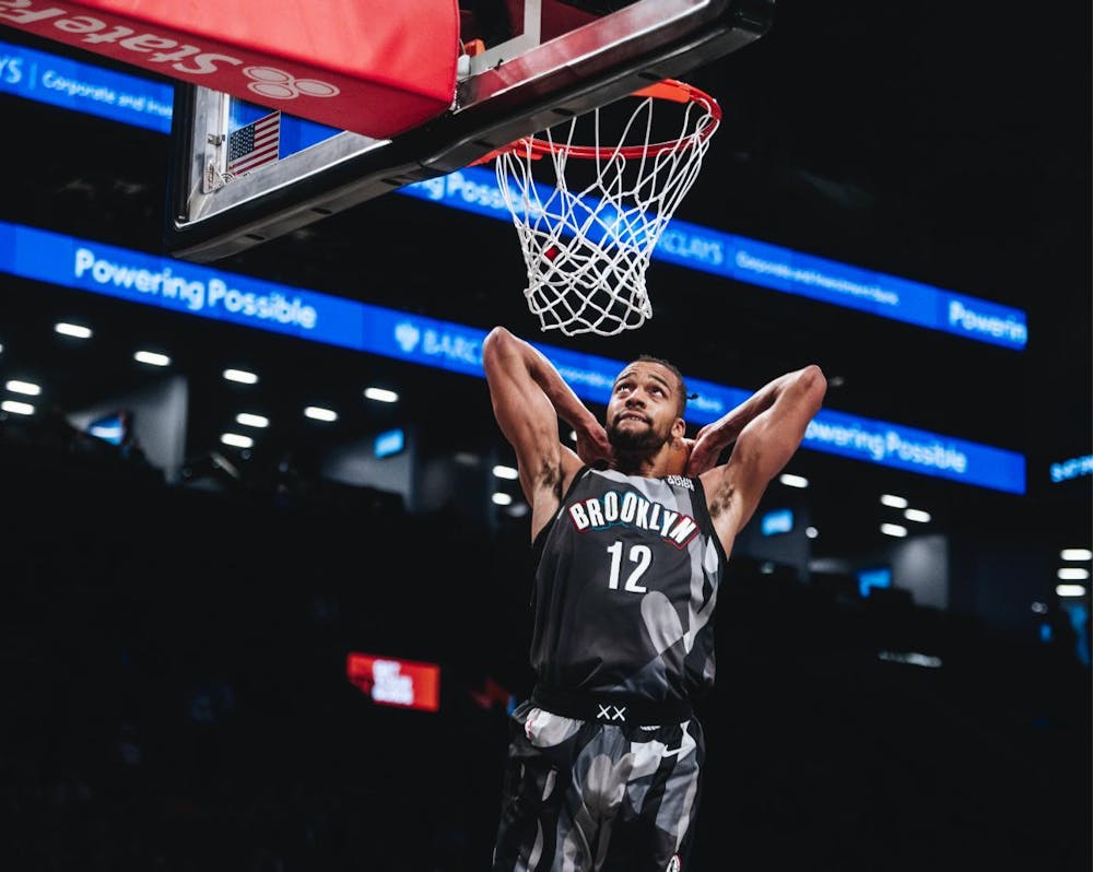 A man wearing a black and gray jersey that says “Brooklyn” dunking a basketball during a game. 