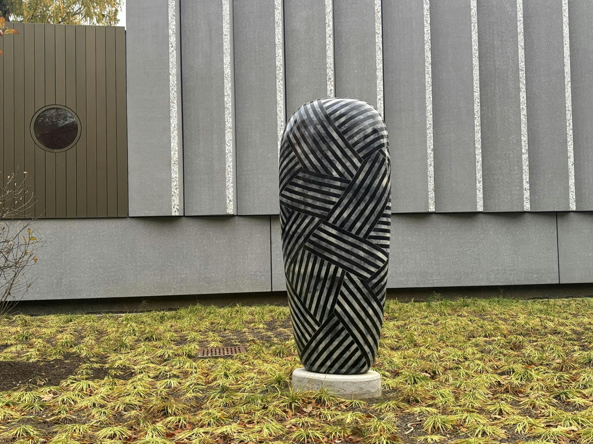 A sphere with black stripes covering its entire surface sits in front of a cement wall of the art museum’s facade.