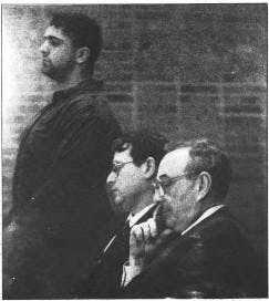 A black and white photograph of student Chris Santoli ’94 , standing up next to his two seated lawyers in suits.
