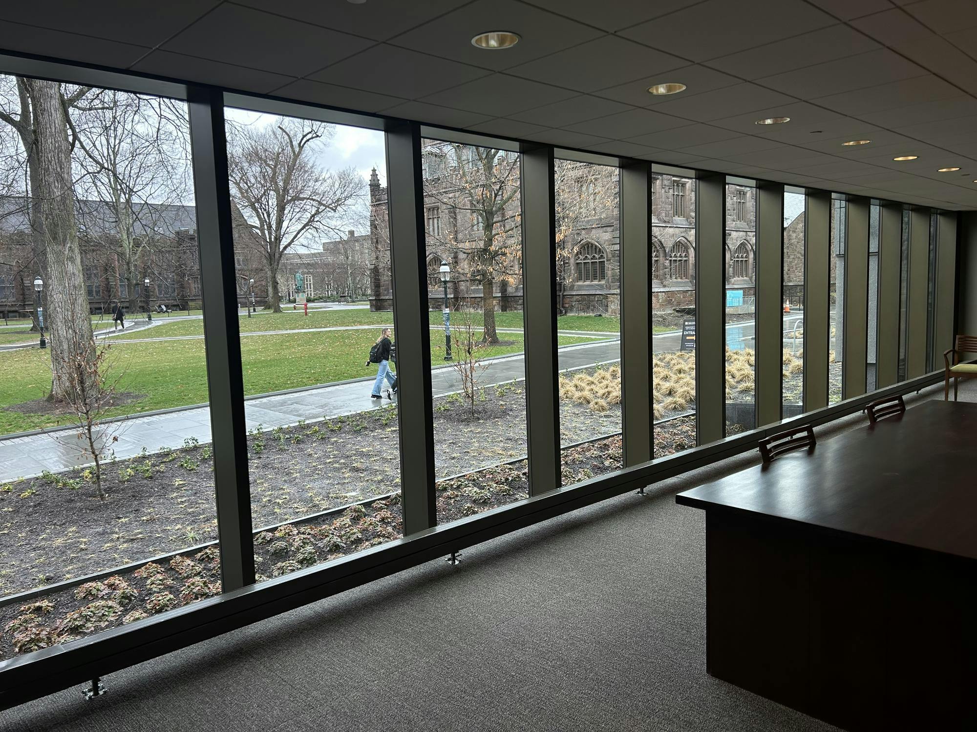 A row of glass panels looks out upon a rainy walkway with students making their way to class. 