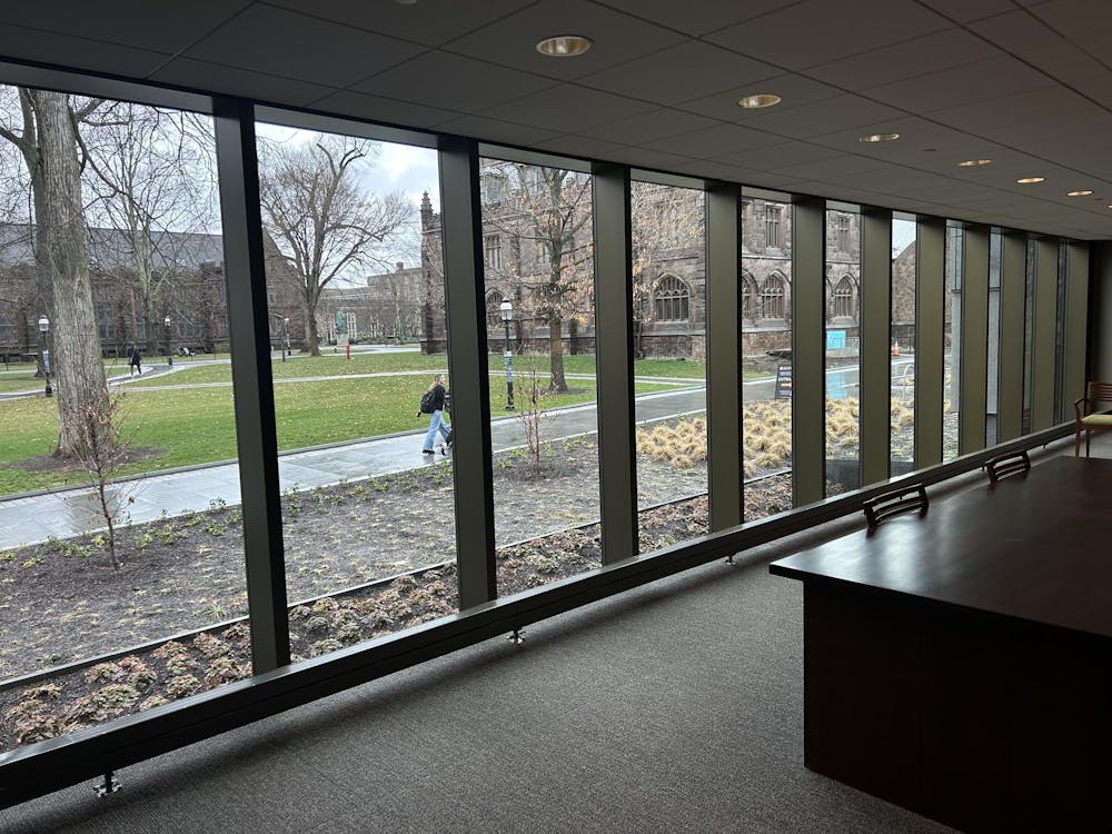 A row of glass panels looks out upon a rainy walkway with students making their way to class. 