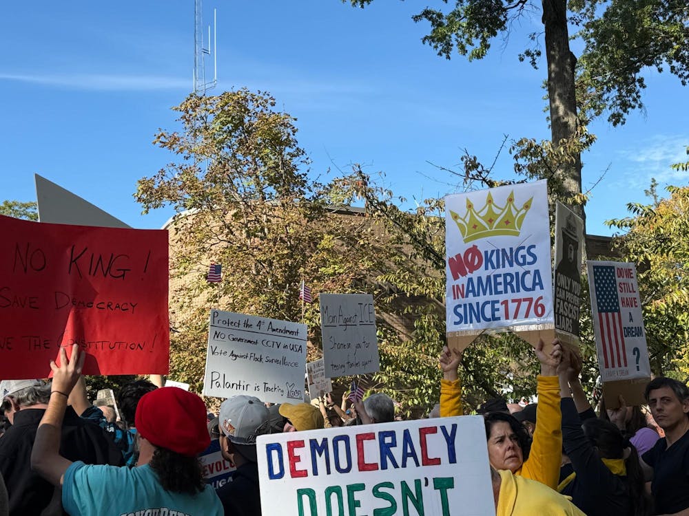 A number of signs raised up at a protest. There are trees in the background.