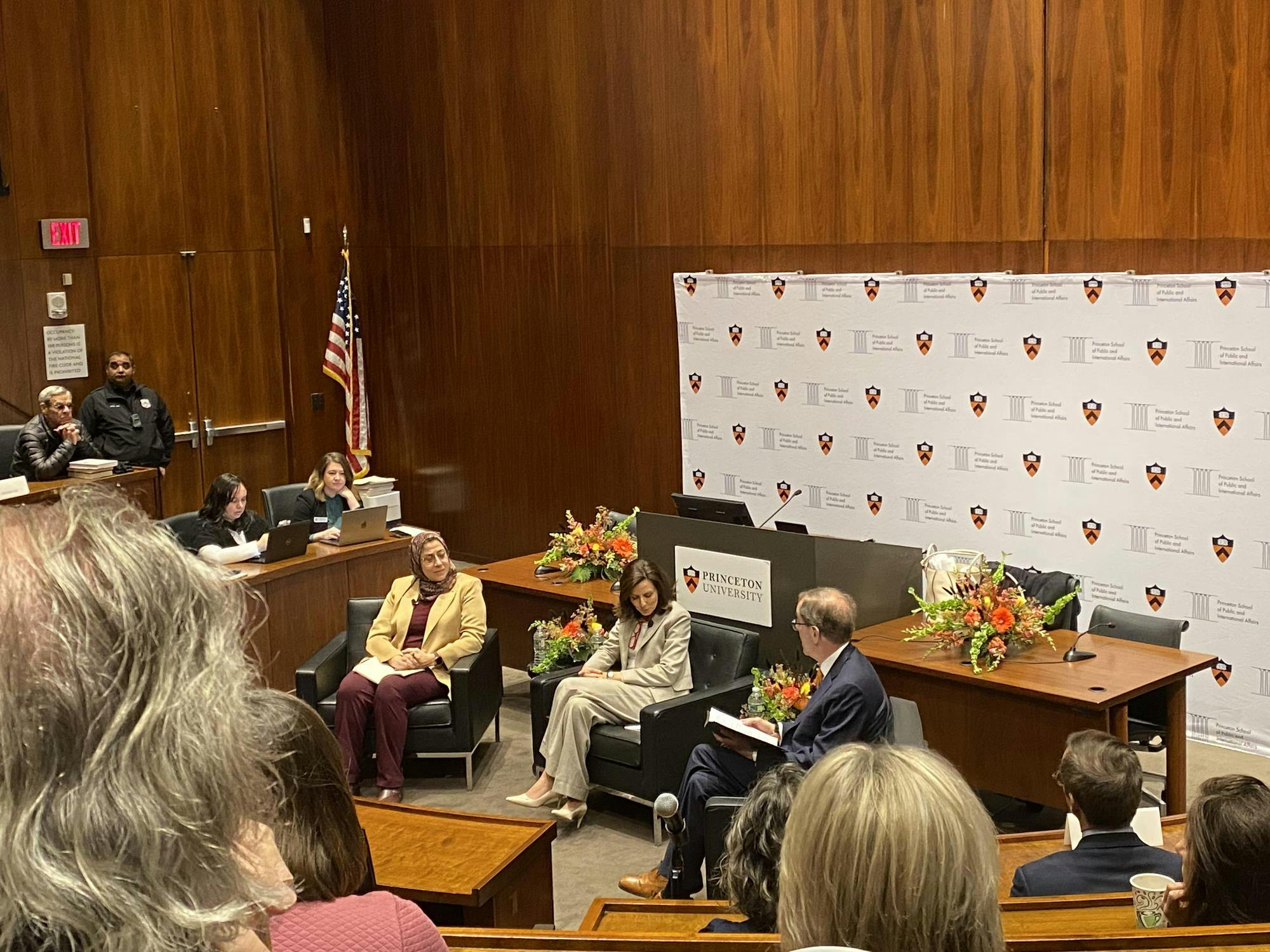Amaney Jamal, Keren Yarhi-Milo, and Christopher Eisgruber sit in front of Robertson lecture hall. Flowers adorn the desk behind them.