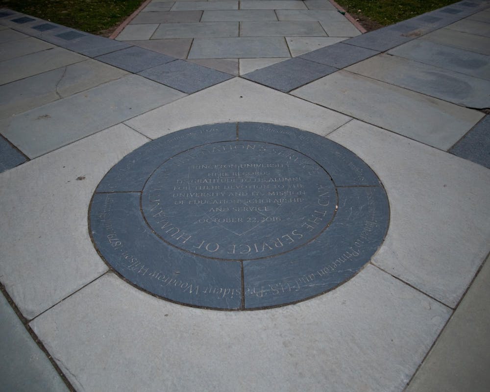 A stone medallion is set into the ground. It has concentric circles of text. The center text reads "In the Nation's Service and the Service of Humanity."