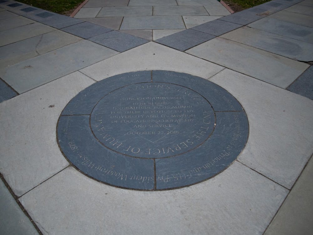 A stone medallion is set into the ground. It has concentric circles of text. The center text reads "In the Nation's Service and the Service of Humanity."