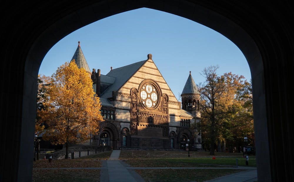 An archway frames a building in the distance with trees with yellow leaves around it