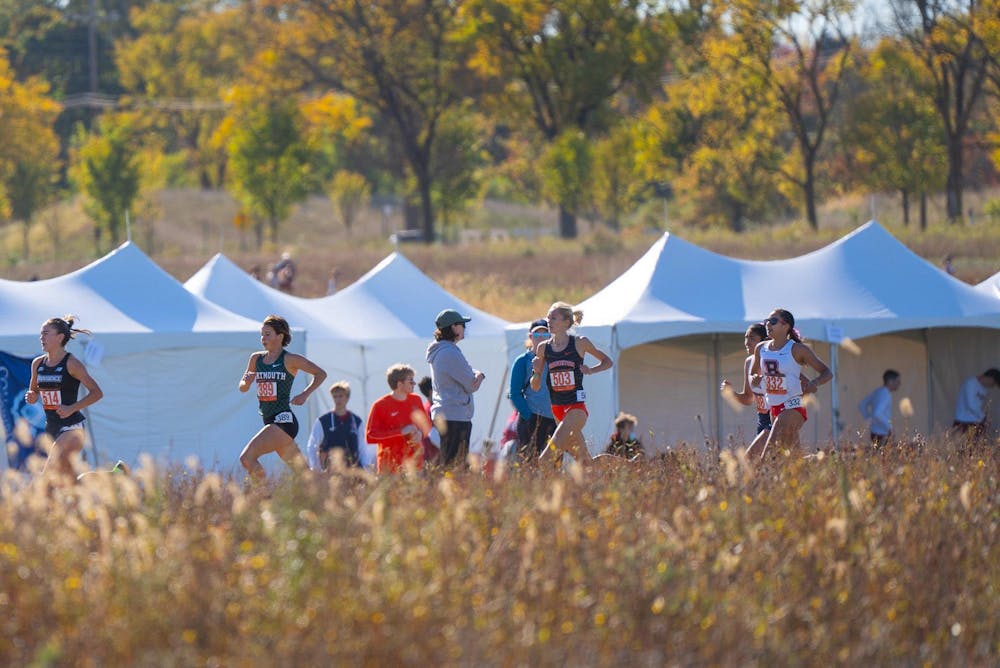 Atop some grass fields, a group of women competing in a cross-country race. 