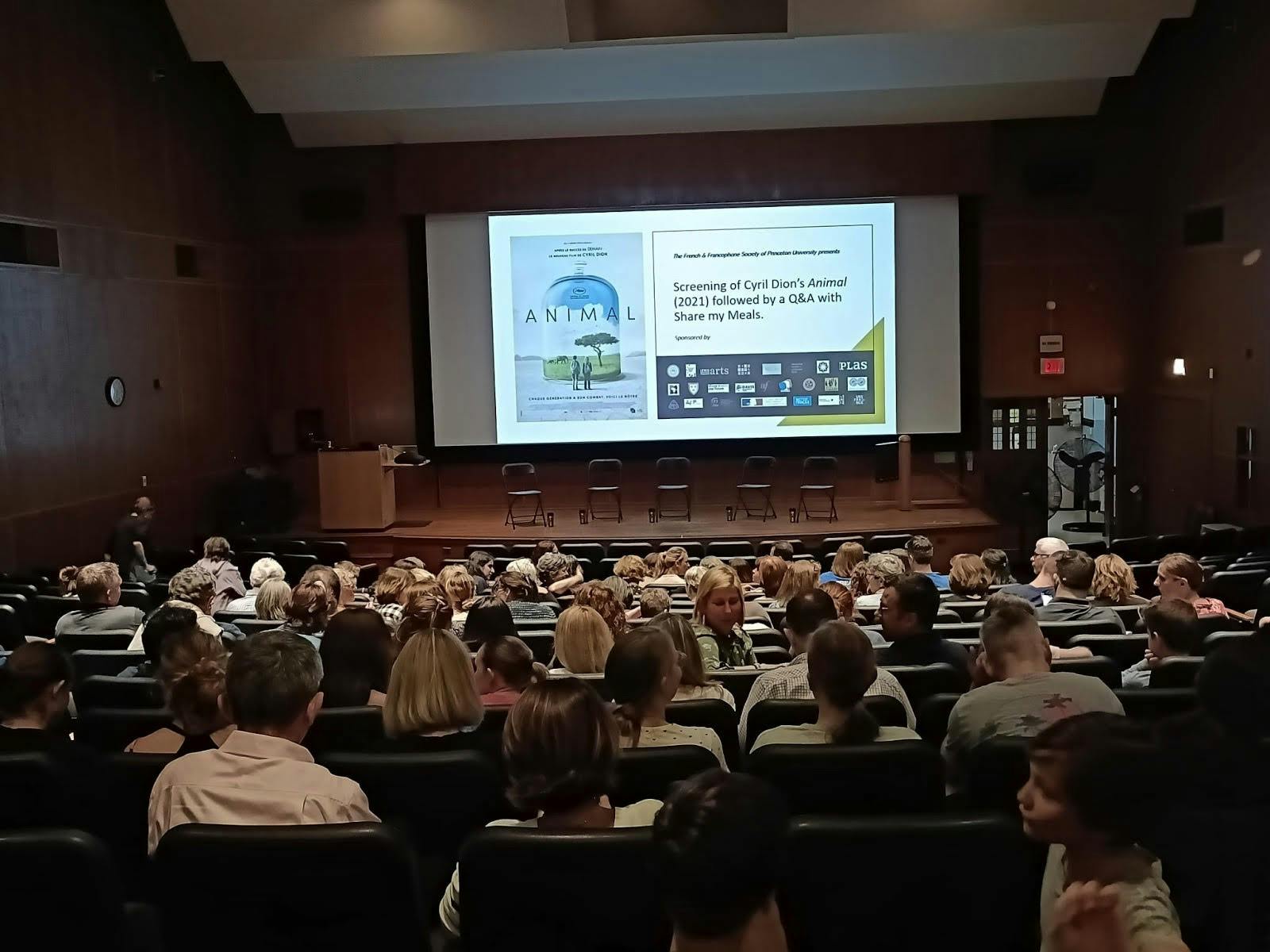 Many people sit in lecture hall in front of a screen which says "Screening of Cyril Dion's Animal followed by Q & A with Share My Meals."