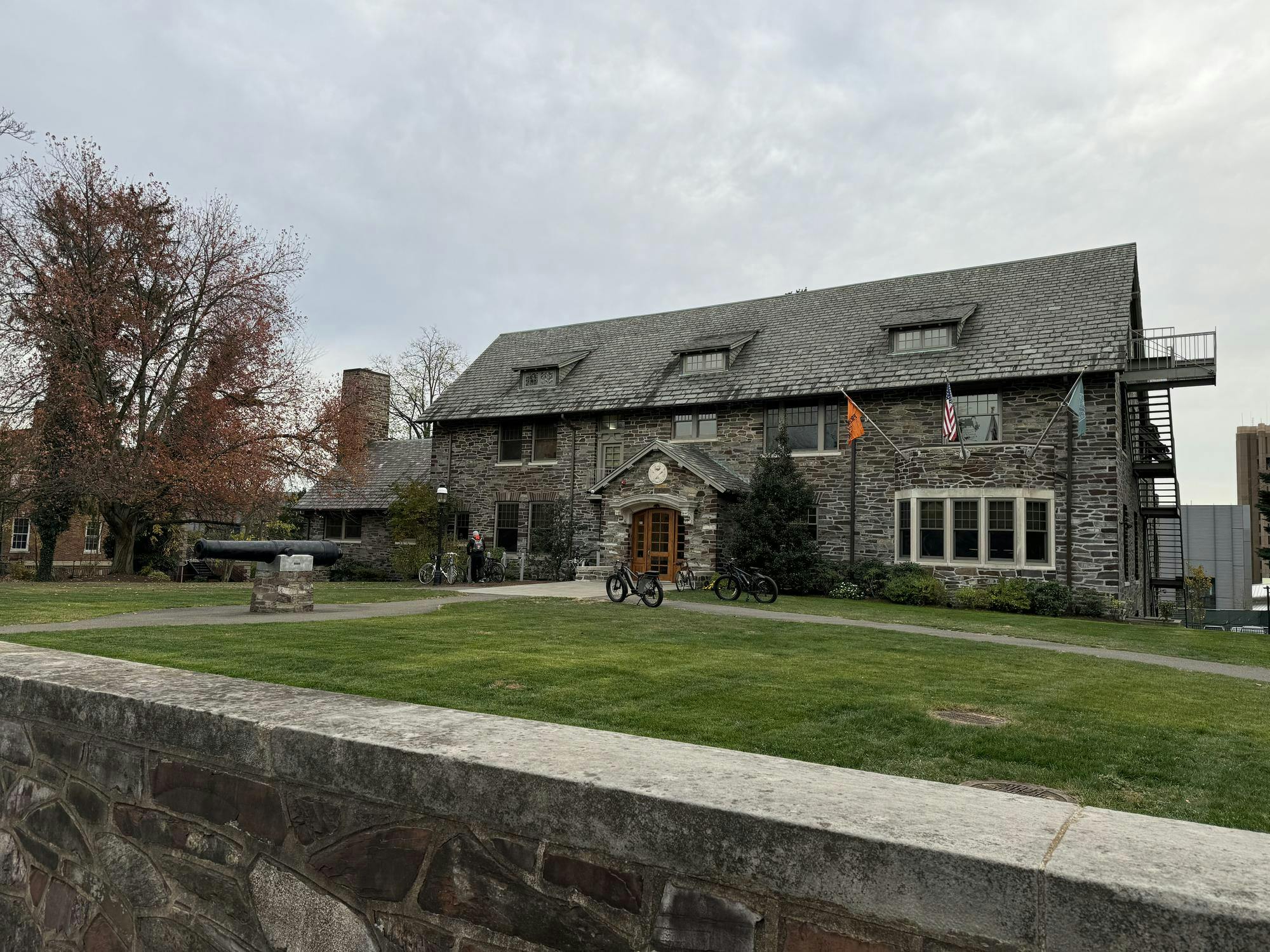 A large gray building sits on a grassy plot of land. A black cannon is in front of the house.