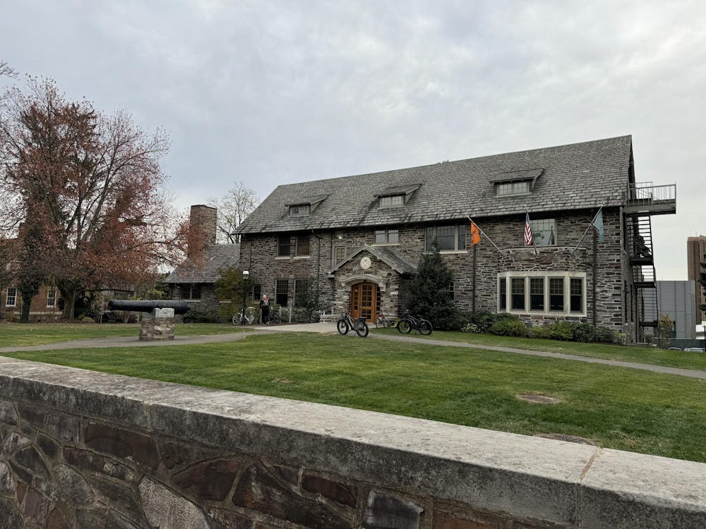 A large gray building sits on a grassy plot of land. A black cannon is in front of the house.