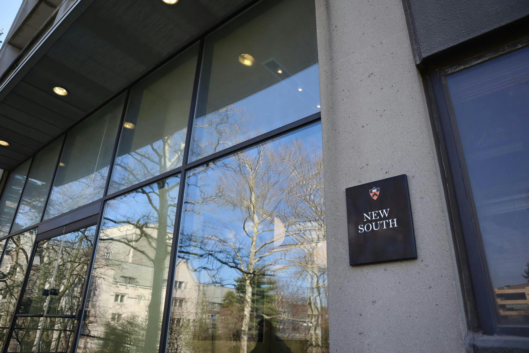 Glass windows reflecting a gothic building and a grey, concrete wall with a black sign.