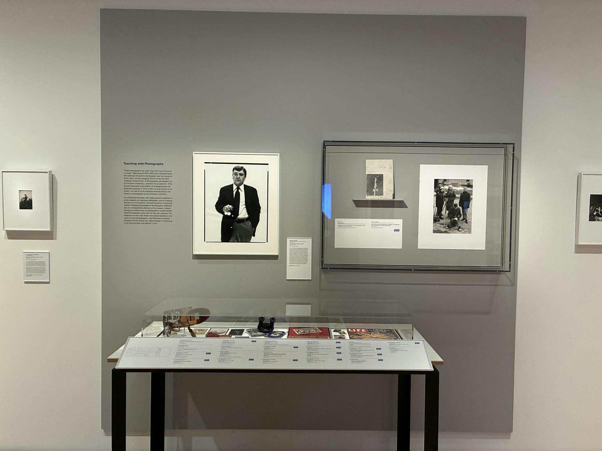 Photos hang on a wall, with a table displaying smaller objects in front.