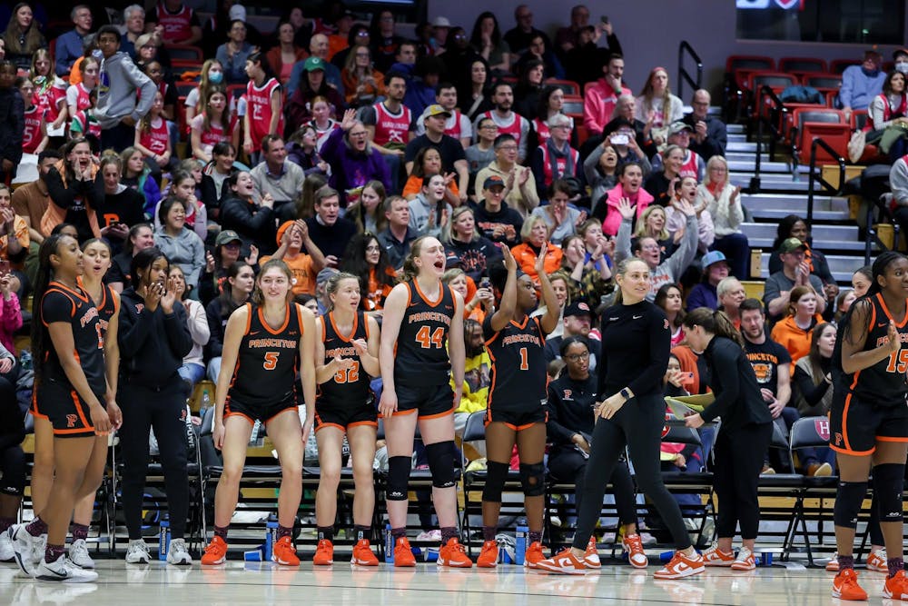 Women in black and orange jerseys celebrate on the basketball court from the bench.