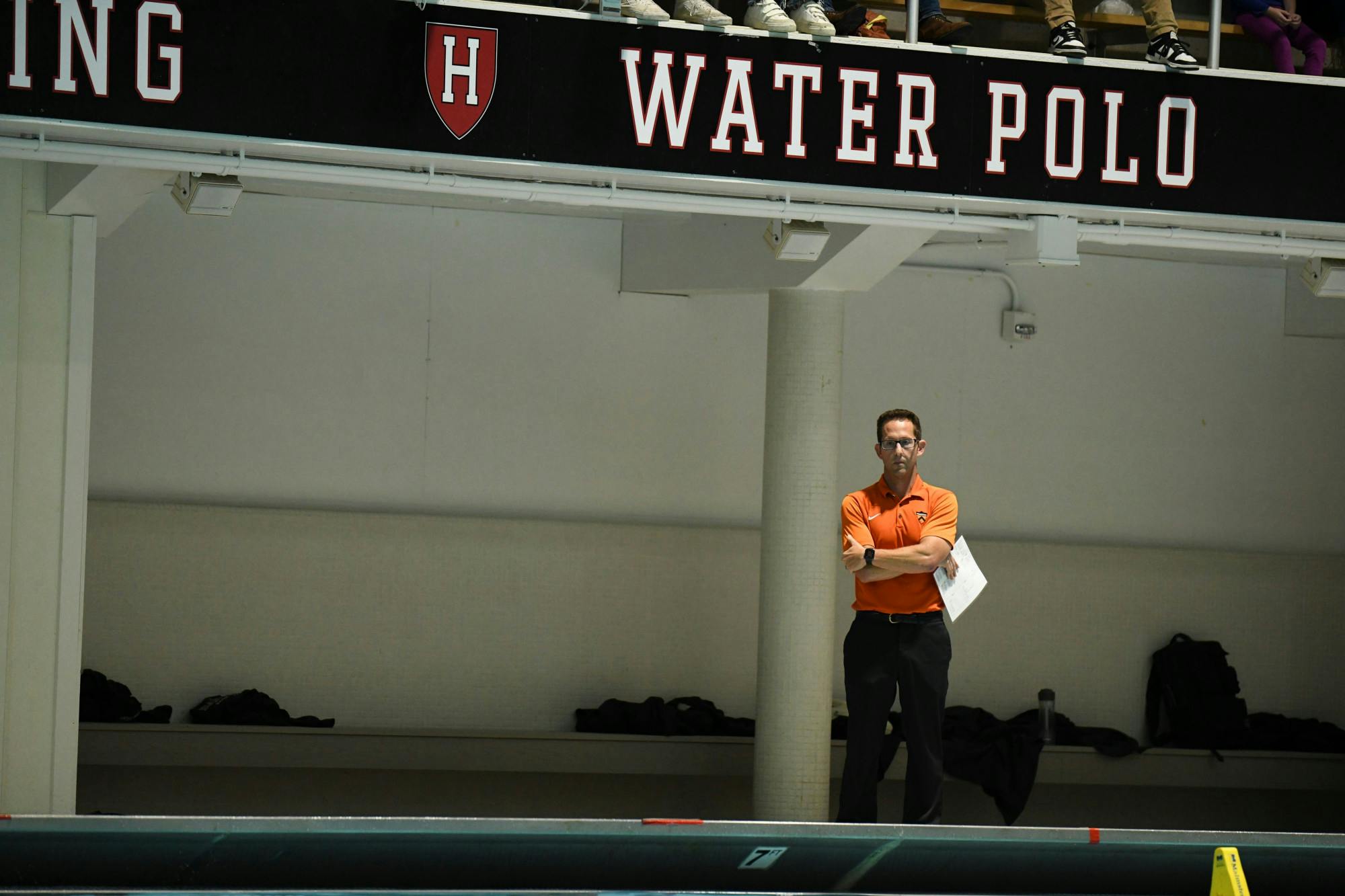 Man with glasses stands with arms crossed next to pole looking down
