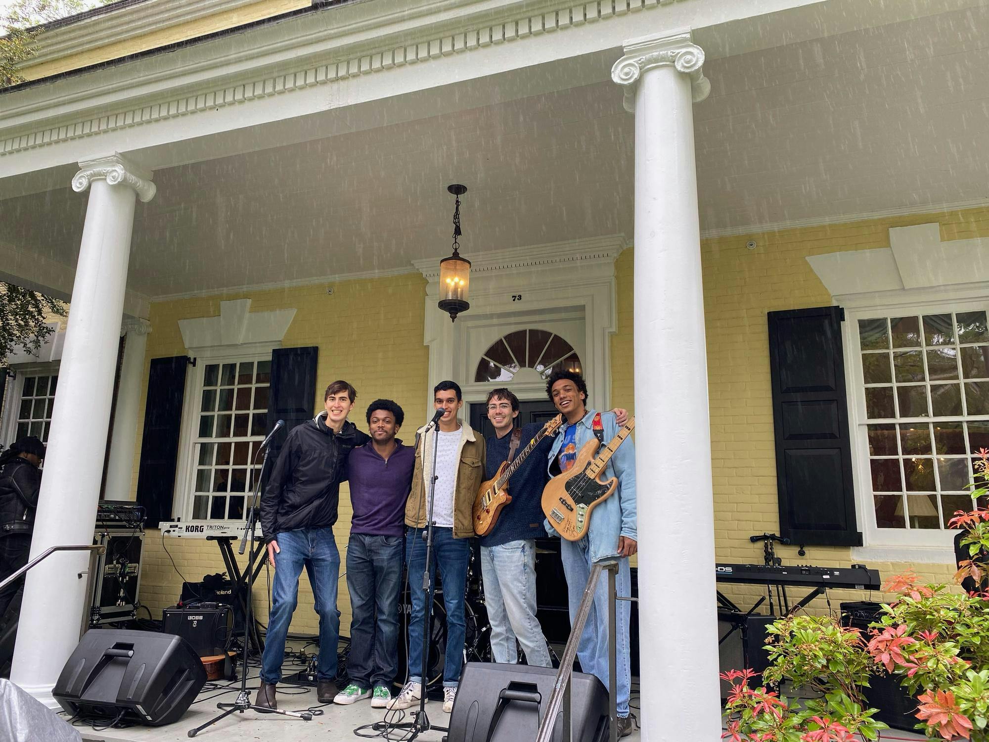 Five musicians standing in front of a yellow house.