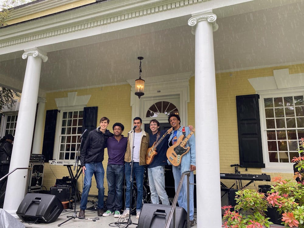 Five musicians standing in front of a yellow house.