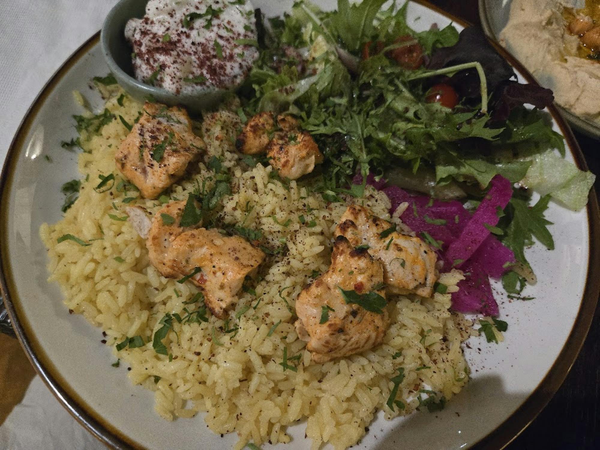 Cubes of grilled chicken over turmeric rice, accompanied by a spring mix salad and yogurt sauce.