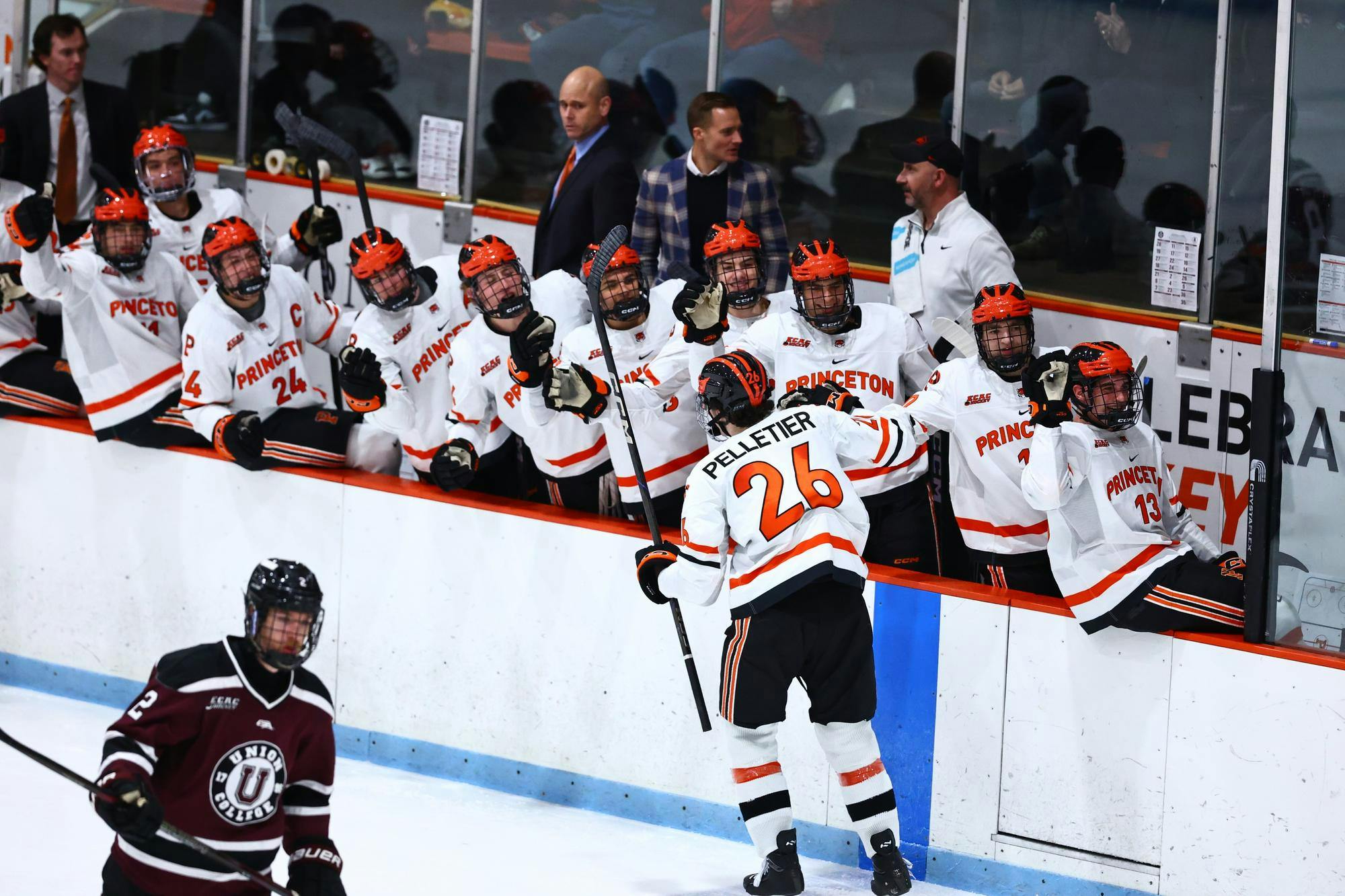 On an ice hockey rink, a player skates while high-fiving his teammates 
