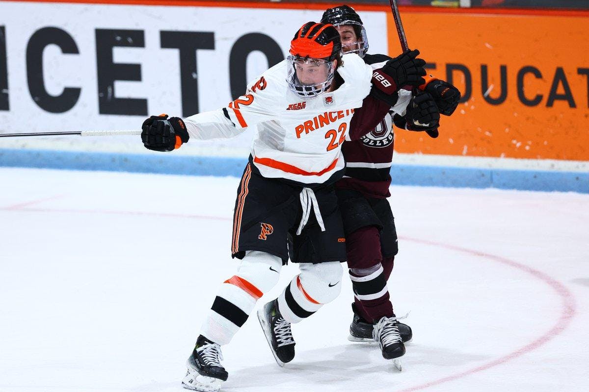 Man in white and orange being held by man in maroon and black jersey. 