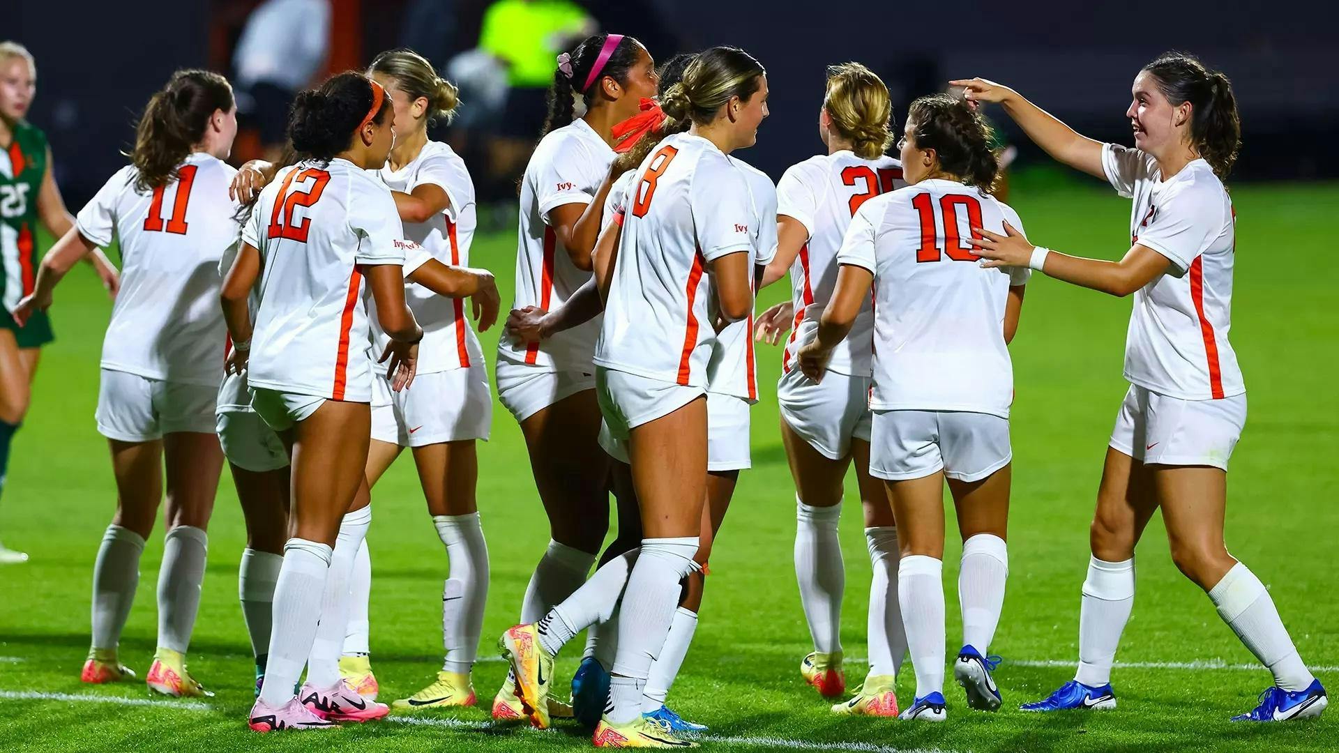Women’s soccer players in orange and white uniforms celebrate after a win 