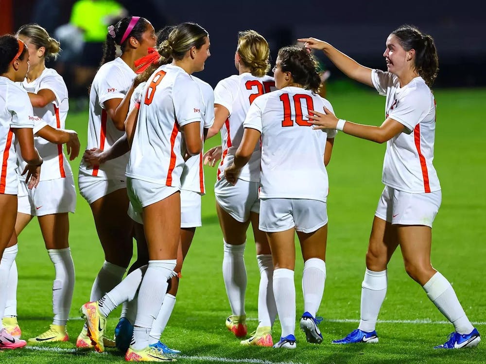 Women’s soccer players in orange and white uniforms celebrate after a win