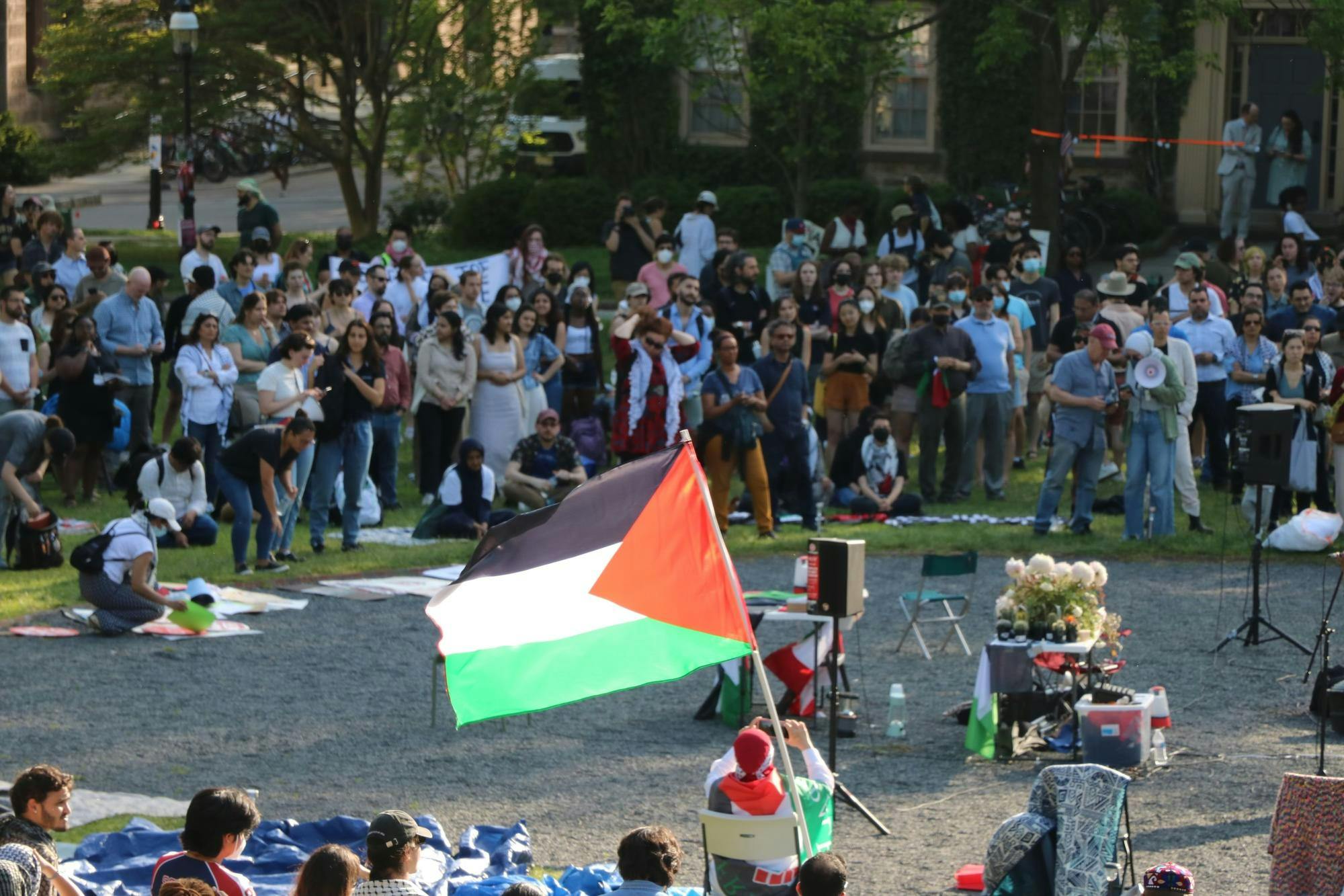A ring of people stand in a circle. In the center, a Palestinian flag waves.