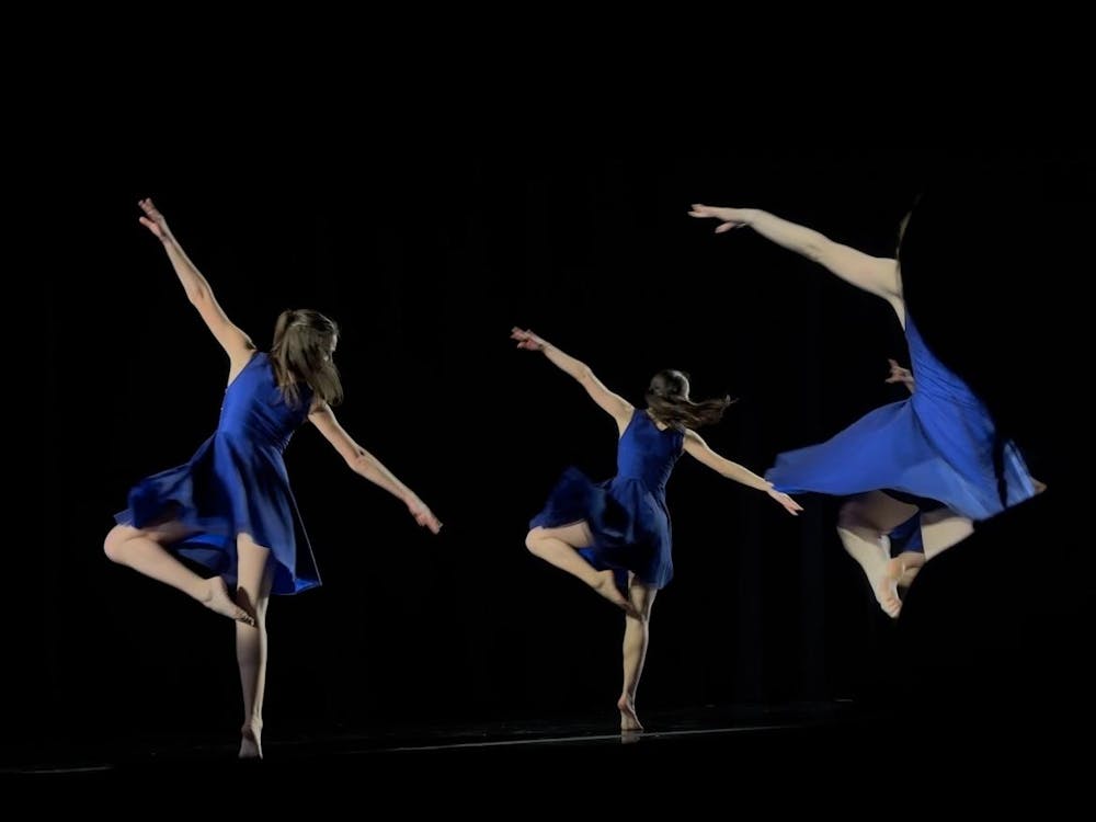 Three dancers in blue dresses do a turn on one leg.