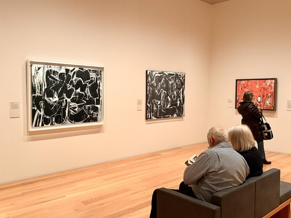 One visitor in a grey shirt and another in a black shirt observe two black and white abstract paintings. 
