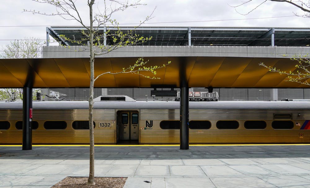 A silver train with a stone pavement ground and one small tree with little leaves.